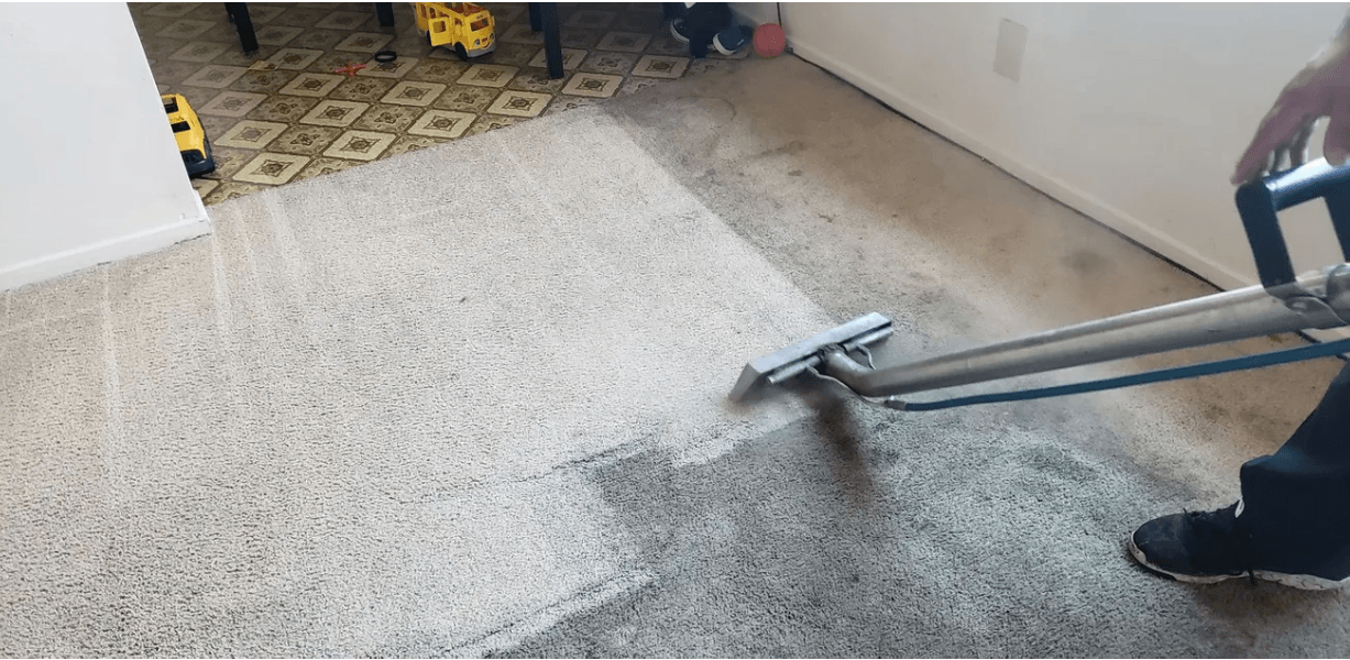 Carpet cleaning machine on light gray carpet in a room, with a person partly visible operating it.