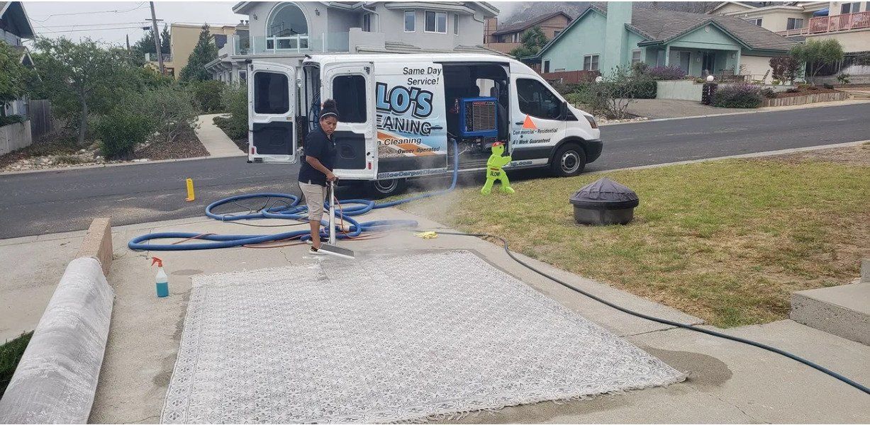 A worker hoses a white gravel bed beside a blue-and-white service van on a suburban street.
