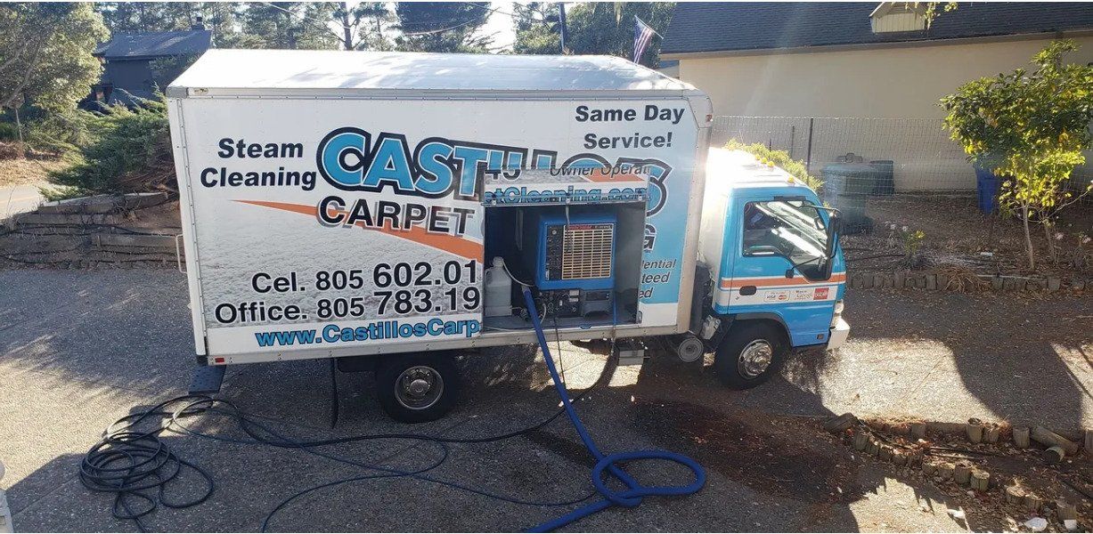 Blue-and-white steam cleaning truck with company logo parked in a driveway near a wall
