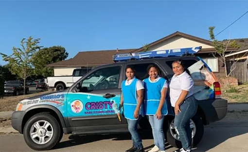 Three people posing beside a blue branded car in a suburban driveway.